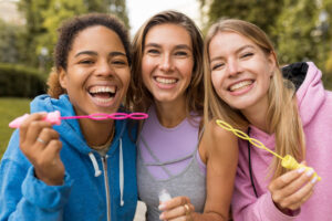 Três adolescentes sorrindo alegremente ao ar livre com aparelhos Invisalign na Clínica Cuidalli, demonstrando a eficácia do tratamento em jovens.