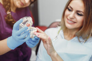 Dentista explica o pós-operatório de implante dentário usando um modelo anatômico para paciente tranquila em consultório na Saúde.