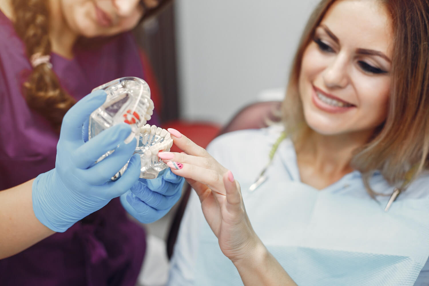 Dentista explica o pós-operatório de implante dentário usando um modelo anatômico para paciente tranquila em consultório na Saúde.
