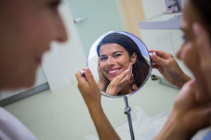 Paciente sorri ao olhar reflexo no espelho durante tratamento para remover manchas brancas ou amareladas nos dentes na Saúde.