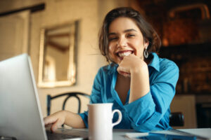 Mulher sorrindo radiante em frente ao notebook, exibindo dentes perfeitos após facetas de resina na Cuidalli Odontologia na Saúde - SP.
